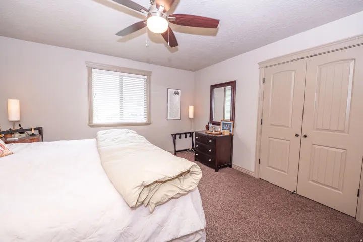 Carpeted room featuring a ceiling fan with integrated lighting, a window with blinds, and two panel-style closet doors