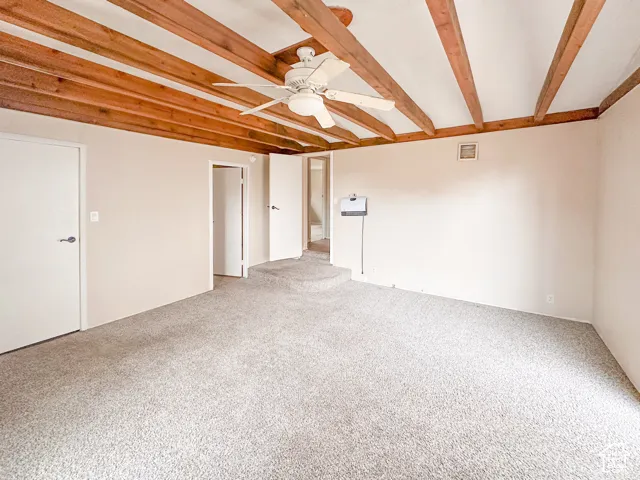 Carpeted room featuring exposed wood beam ceiling, ceiling fan with light fixture, neutral wall paint, and multiple doorways