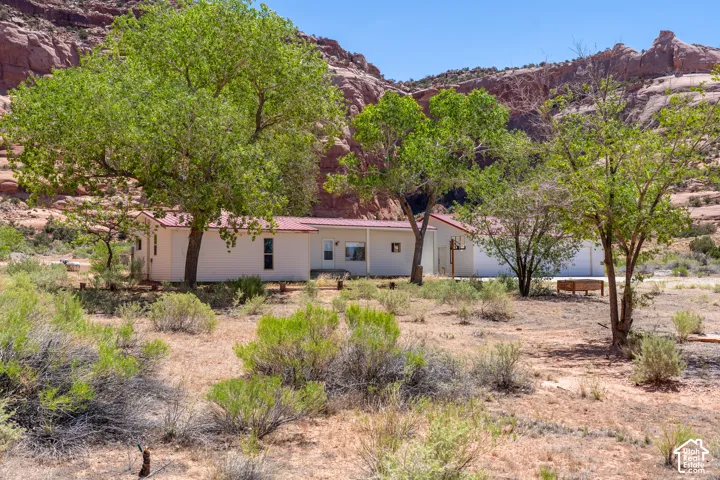 White single-story residence with a red roof, surrounded by mature green trees and desert landscaping