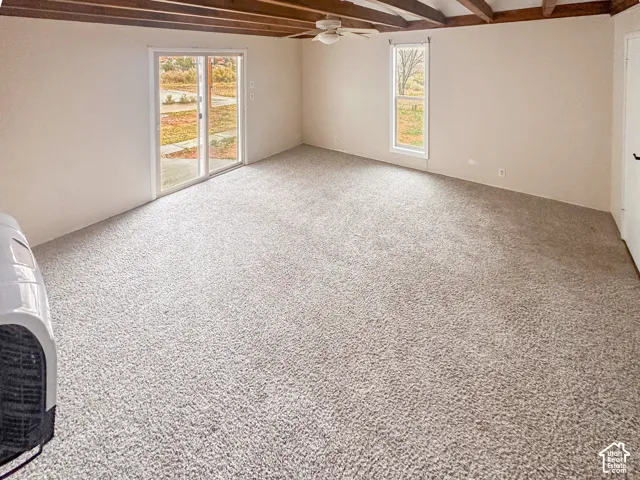 Spacious room featuring exposed ceiling beams, light-colored carpeting, and a ceiling fan