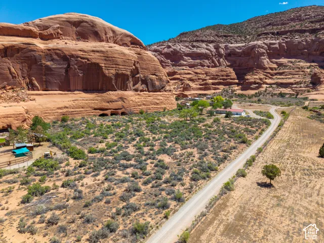 Expansive desert landscape featuring natural rock formations, a winding unpaved road, and distant residential structures