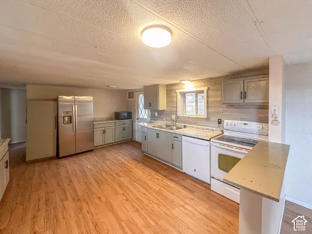 Spacious kitchen featuring wood-finish flooring, light-toned cabinetry, light-colored countertops, a tile backsplash, and a built-in breakfast bar