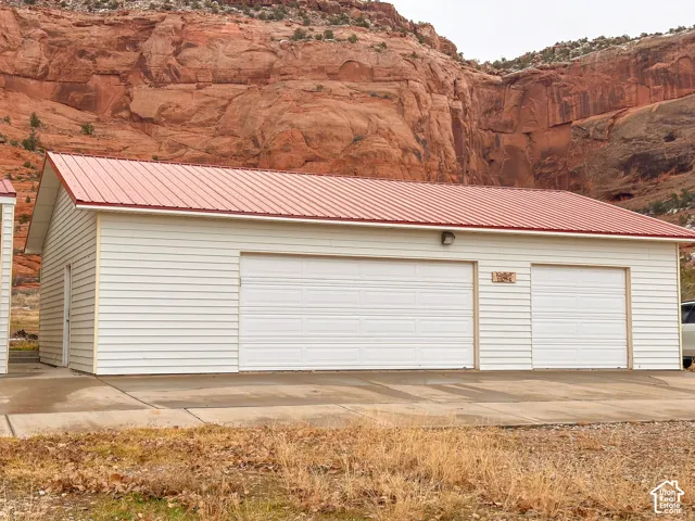Detached multi-bay garage structure featuring a red corrugated metal roof, white horizontal siding, and multiple white garage doors