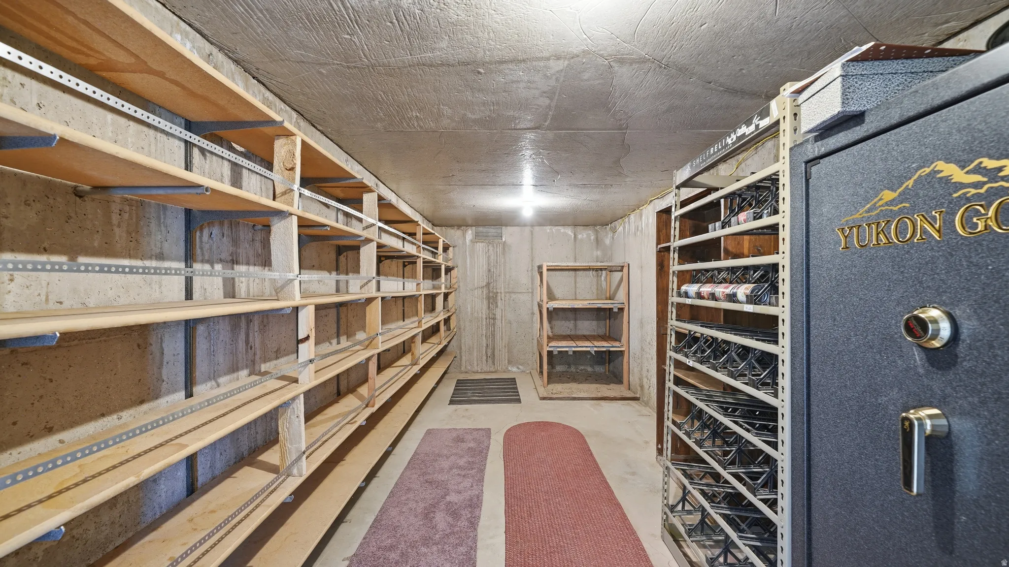 Cold storage  room featuring extensive built-in wooden shelving, concrete walls, concrete ceiling, and additional freestanding shelving