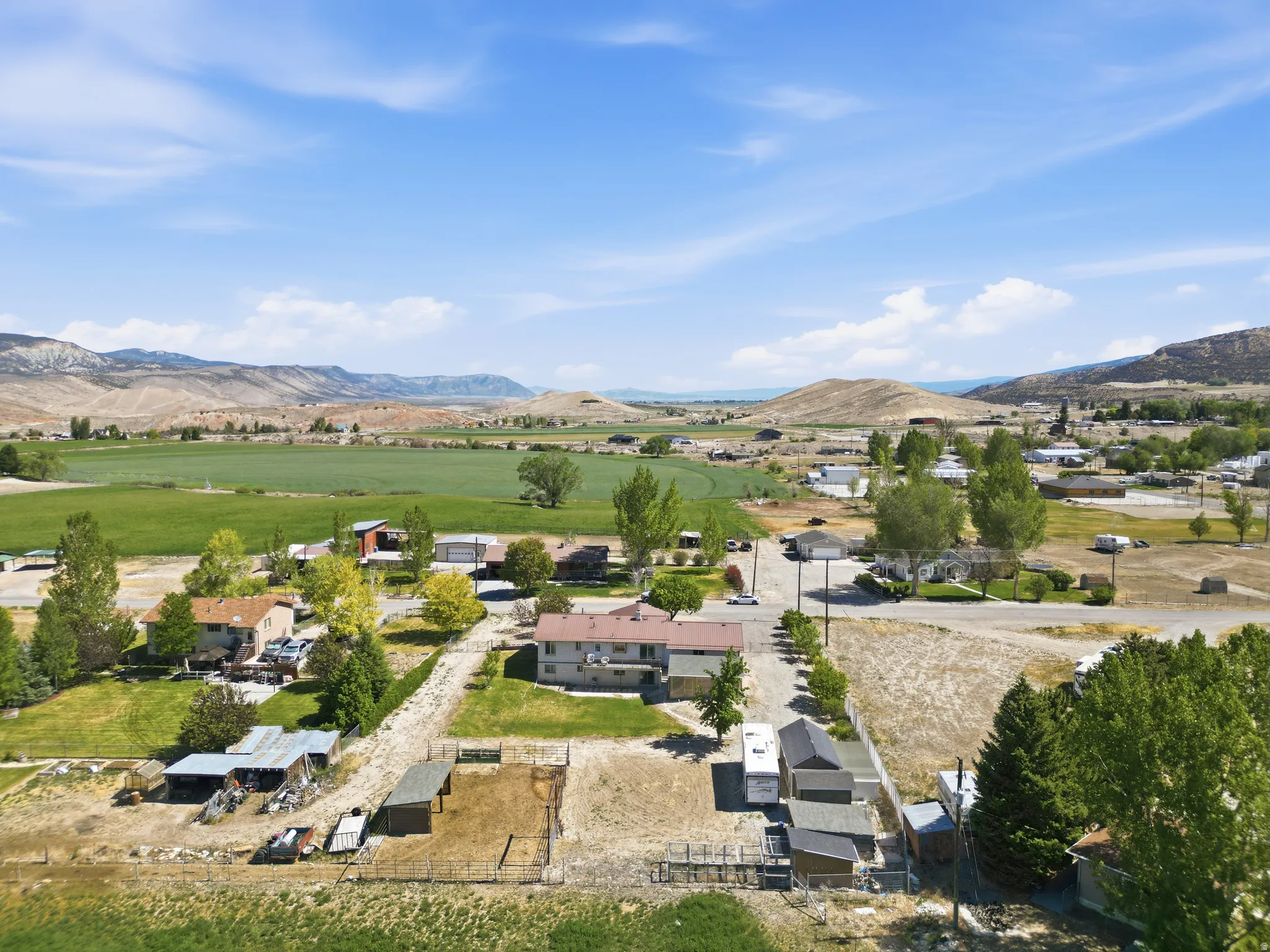 Expansive rural property featuring multiple outbuildings, fenced enclosures, and a surrounding natural landscape with distant hills and green fields