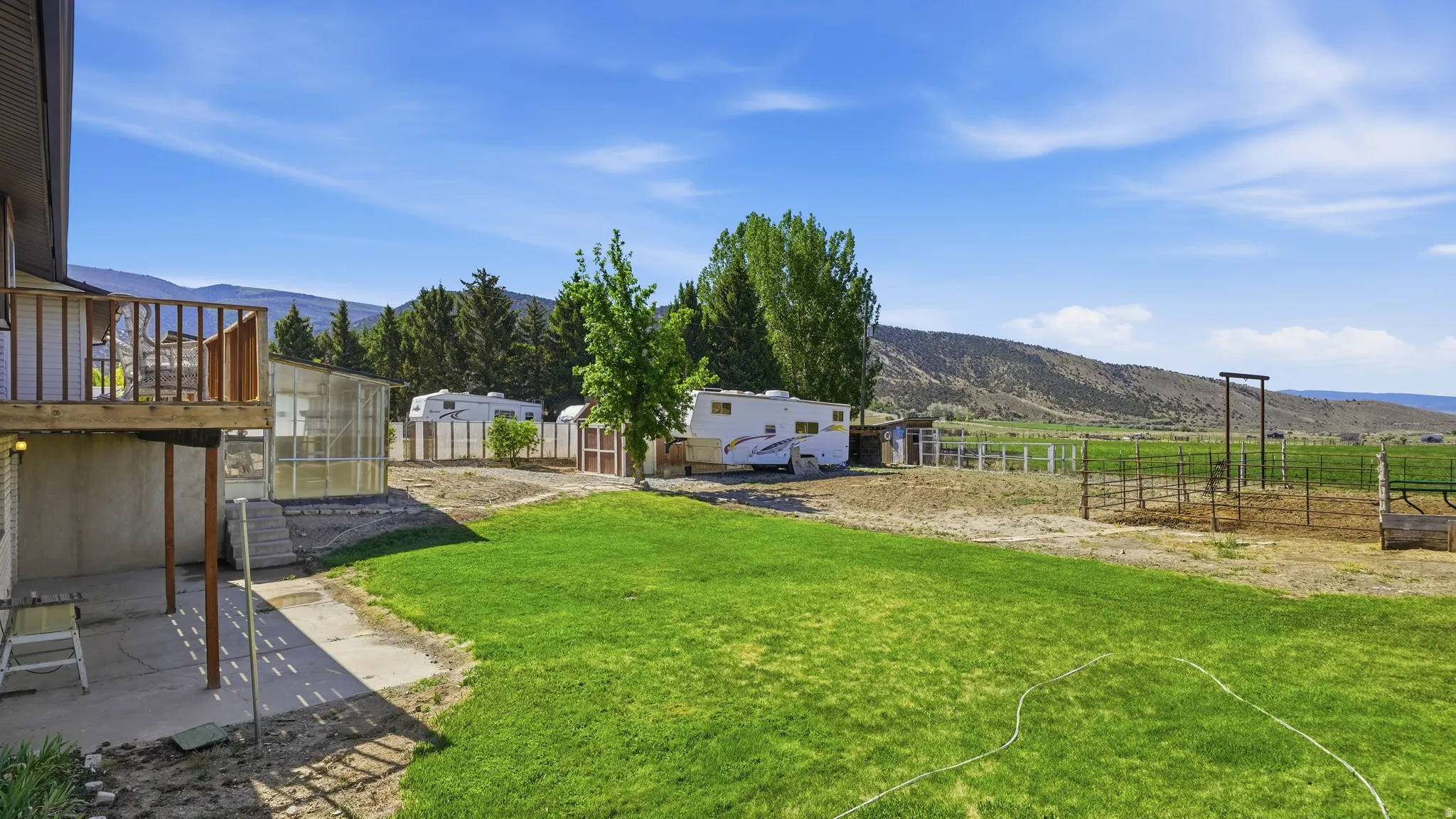 Expansive backyard with a manicured lawn, concrete patio, and a transparent greenhouse structure