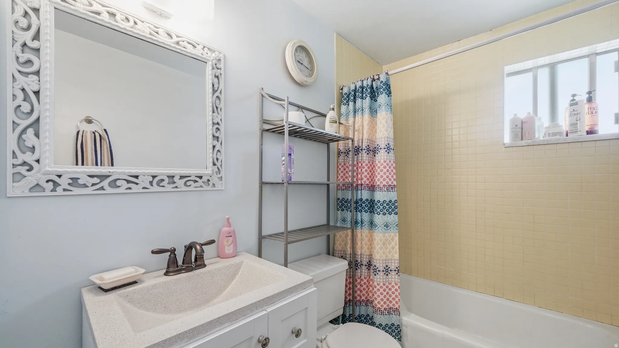 Bathroom featuring a vanity with an integrated sink and bronze-finish faucet, a decorative framed mirror, and a tub with tiled surround
