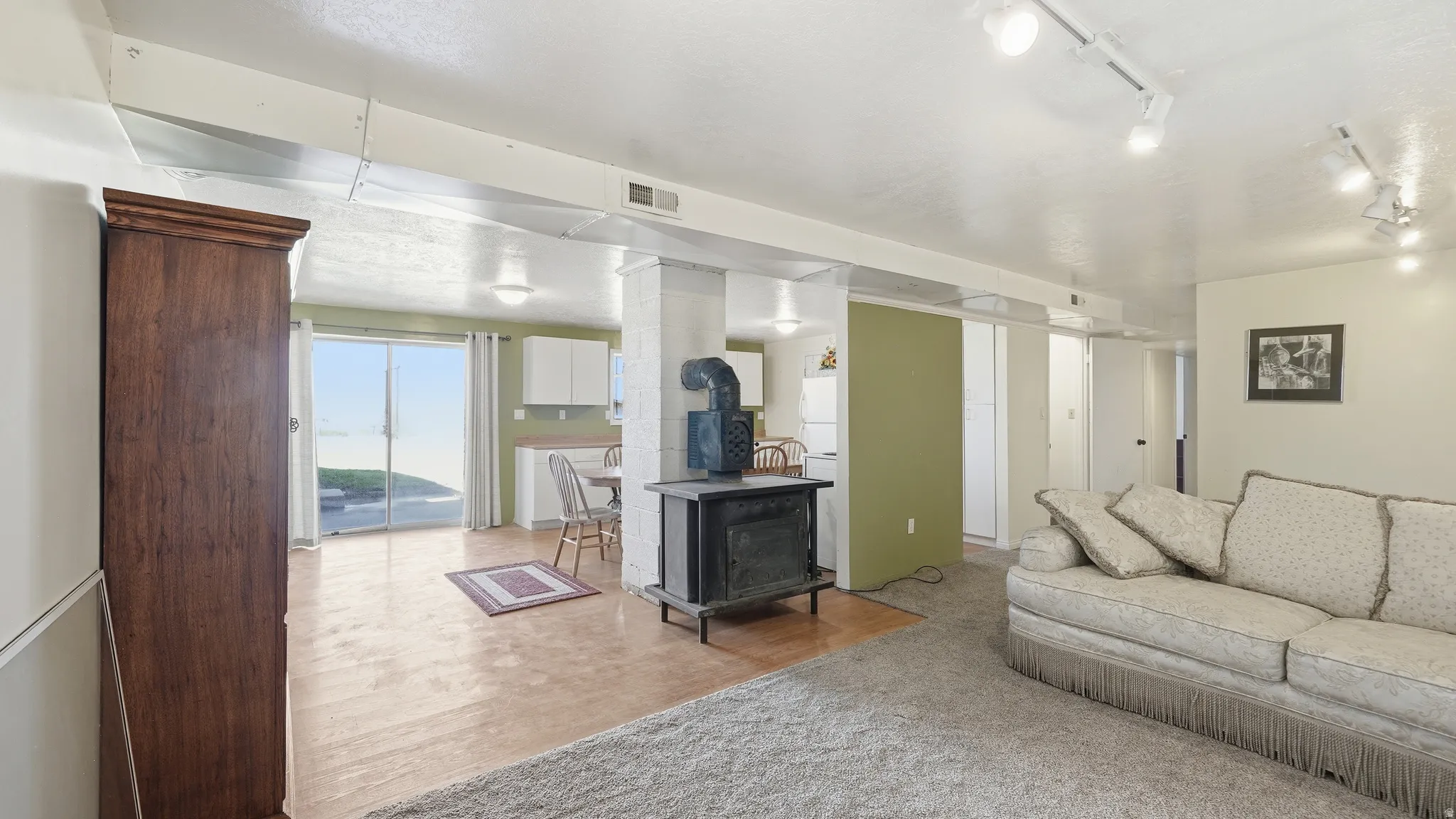 Spacious open-concept area featuring a wood-burning stove, track lighting, and a sliding glass door leading to the exterior