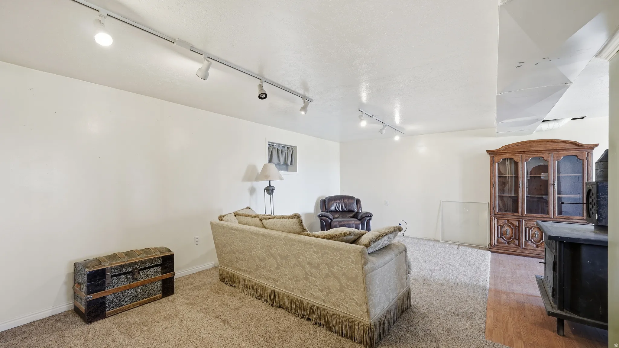 Spacious interior room featuring white walls, track lighting, and a combination of carpet and wood-finish flooring