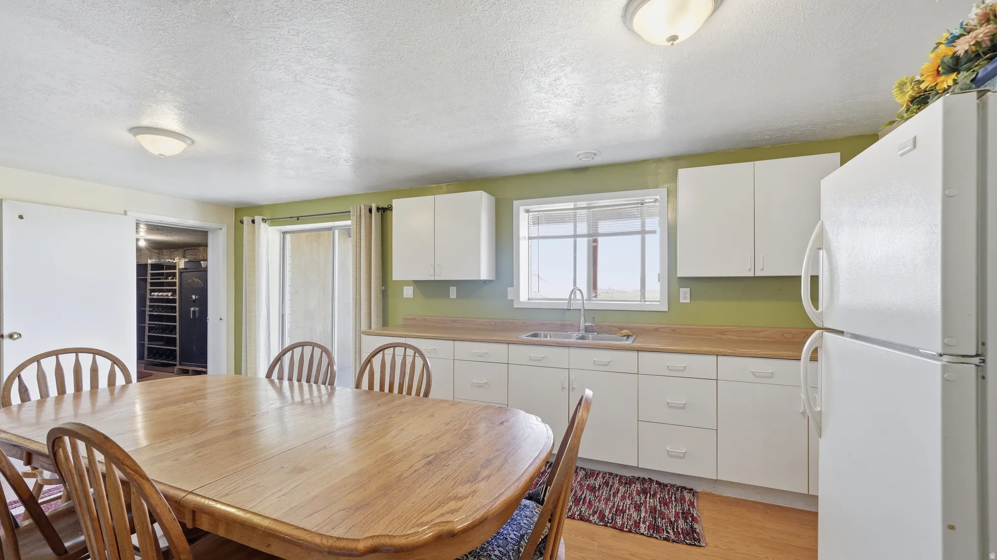 Galley-style kitchen featuring white cabinetry, light wood-finish countertops, stainless steel sink, and white appliances