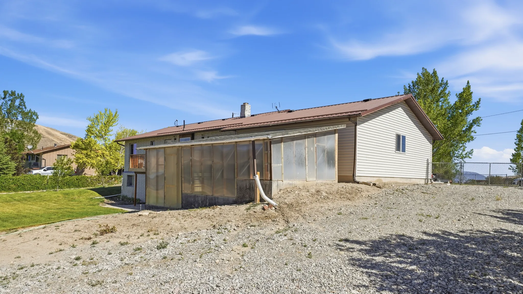 Property exterior featuring a attached greenhouse structure, light-colored siding, a brown roof, and a gravel foreground