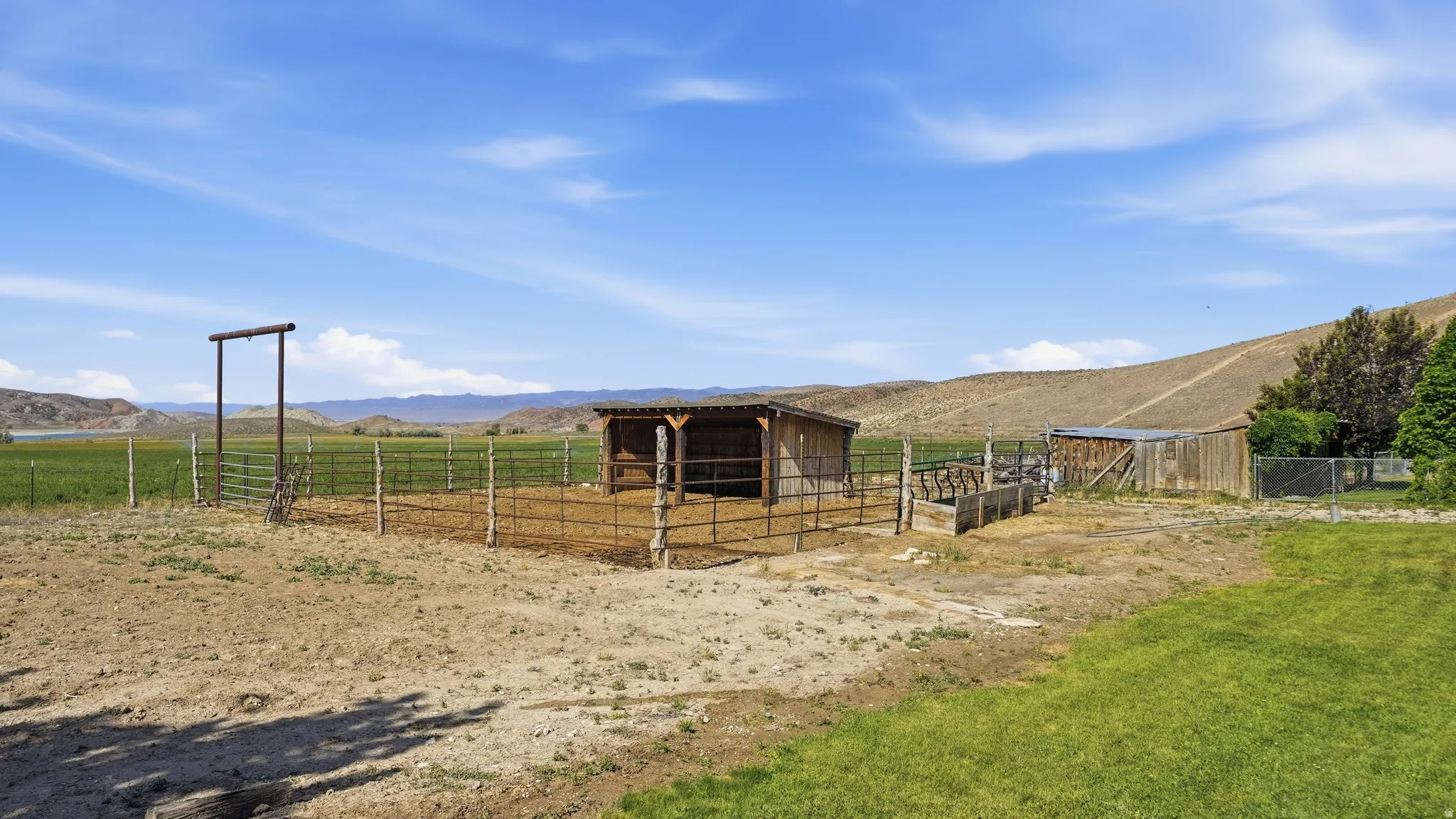 Expansive property featuring a rustic shelter, fenced enclosures, and a large metal gate
