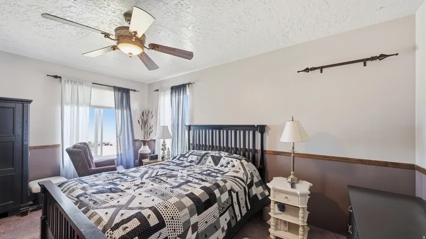Spacious bedroom featuring large windows providing natural light, a ceiling fan with integrated lighting, and a two-tone wall finish with a decorative wood accent rail
