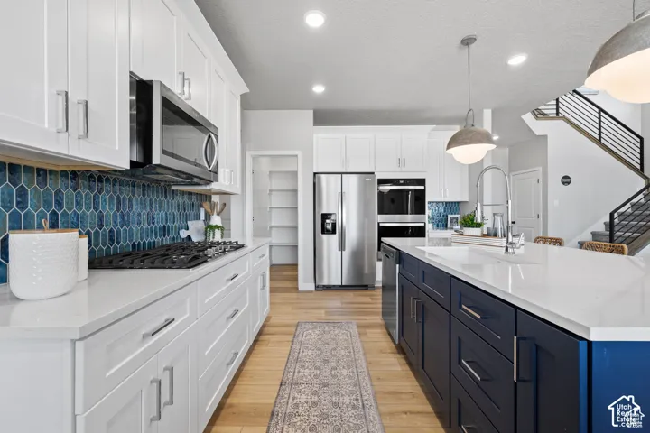 Open-concept kitchen featuring white shaker cabinetry, white countertops, and a blue hexagonal tile backsplash