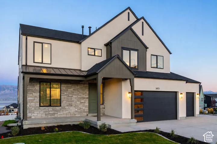 Contemporary two-story exterior featuring a mix of stucco and stone cladding, a prominent gabled roofline, and a modern garage door with frosted glass panels
