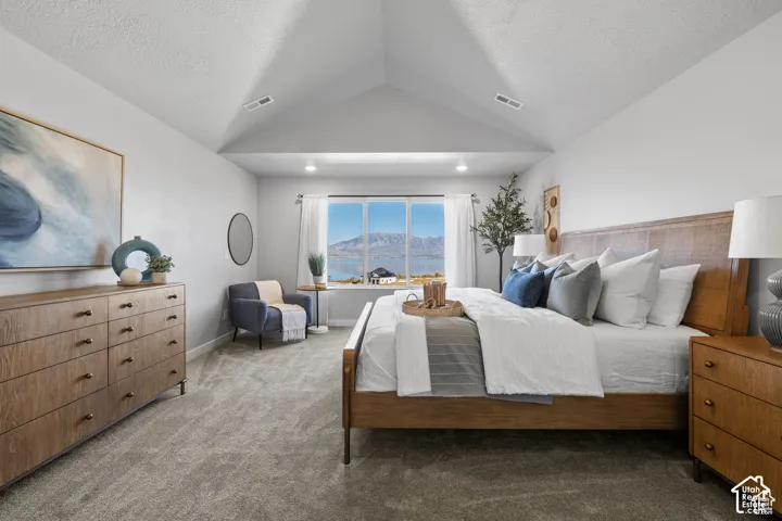 Vaulted ceiling bedroom featuring a large window with mountain and water scenery, light gray carpet, and recessed lighting