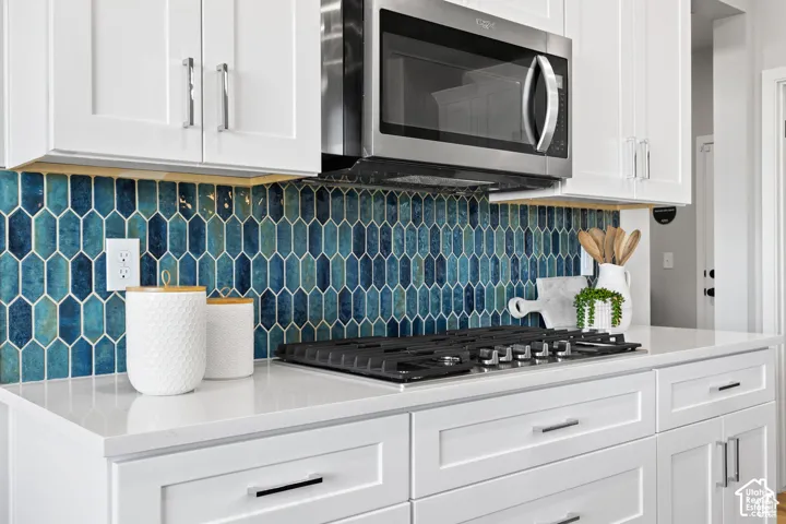 Kitchen featuring white shaker cabinetry, stainless steel microwave, gas range cooktop, quartz countertops, and a blue picket tile backsplash