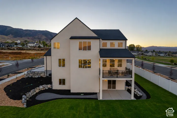 Contemporary two-story exterior with a covered balcony, lower patio, and expansive lawn