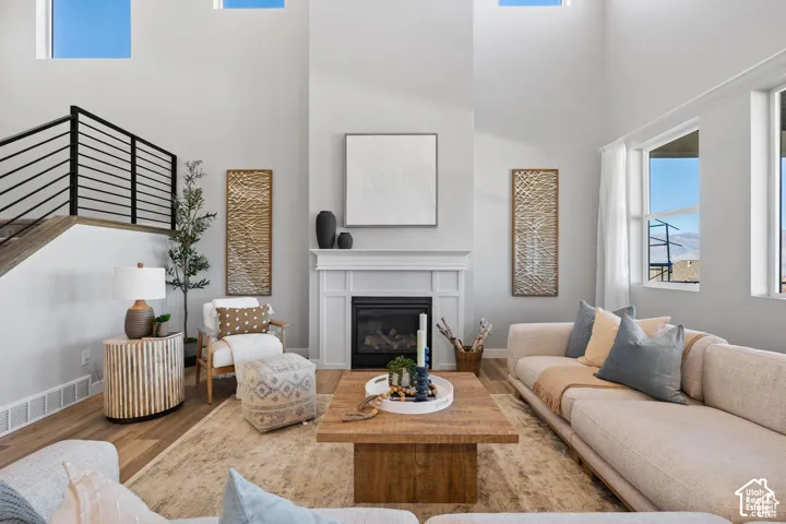 Expansive living space featuring a floor-to-ceiling fireplace, tall windows, wood-finish flooring, a contemporary staircase with black railings, and skylights providing abundant natural light