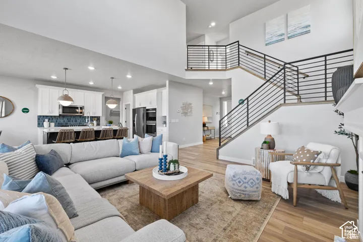 Open-concept living space with high ceilings, wood-finish flooring, a modern kitchen with a blue tile backsplash, stainless steel appliances, and a central island with pendant lighting