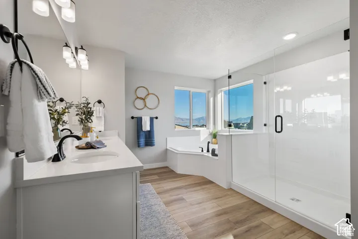 Bathroom featuring a dual vanity with undermount sinks, a corner soaking tub, a frameless glass shower enclosure, wood-finish flooring, and multiple windows