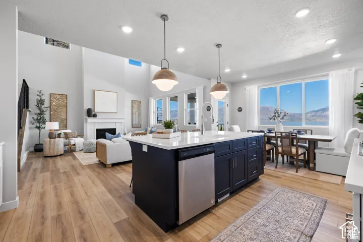 Open-concept living space featuring wood-finish flooring, a two-story vaulted ceiling, and a fireplace with a white mantel