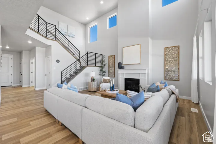 Two-story living area featuring wood-finish flooring, a contemporary staircase with black metal railings, a classic white fireplace, and multiple windows allowing abundant natural light