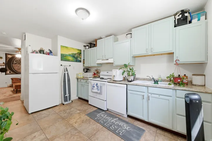 Kitchen featuring light blue cabinetry, mottled countertop surfaces, a white sink, and tile flooring