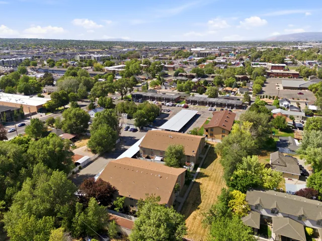 Aerial perspective showcasing a residential area with mature trees, multiple buildings with brown shingle roofs, and paved parking areas