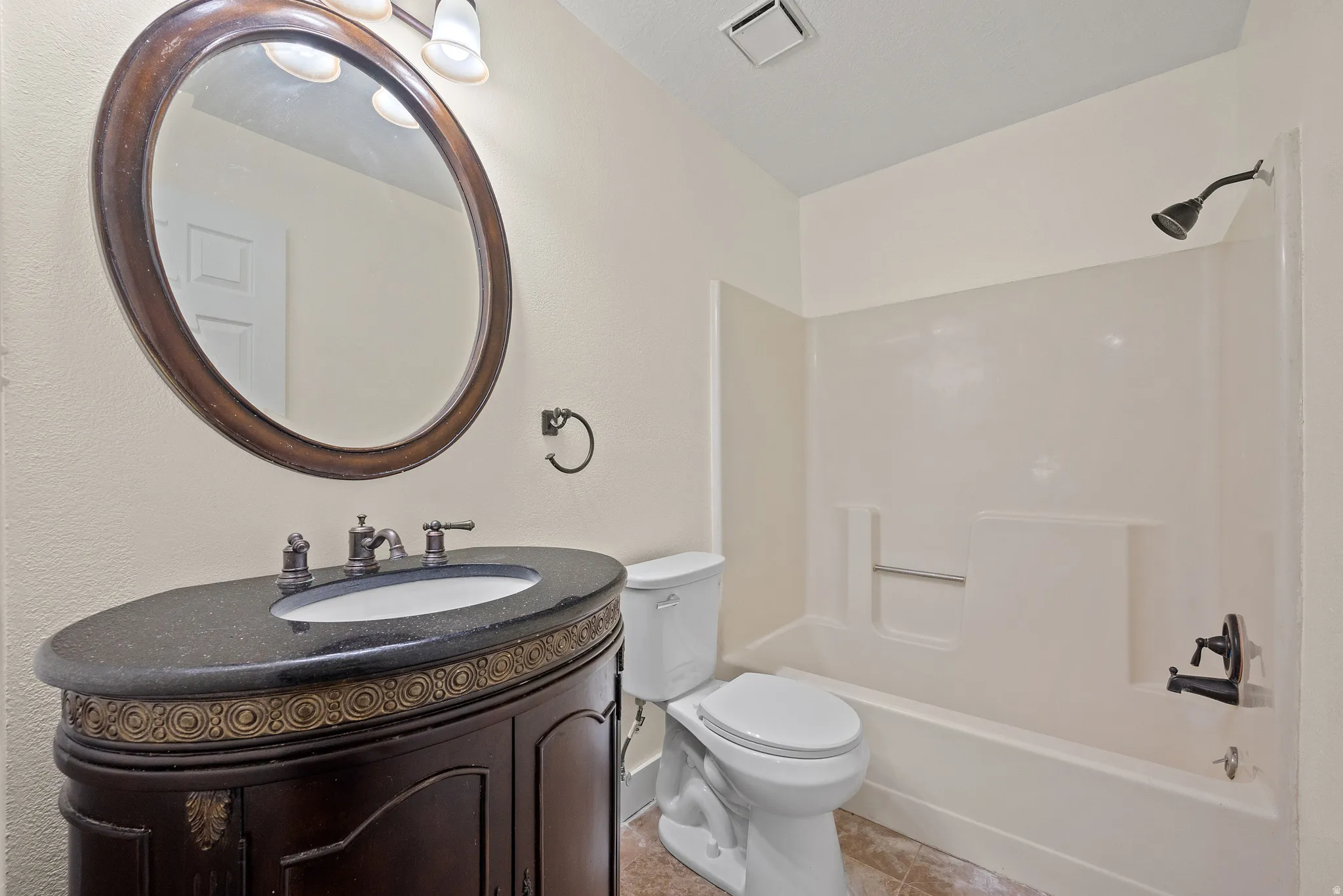 Bathroom featuring a dark wood vanity with ornamental detailing, a black speckled countertop, and an oval mirror with a matching wood frame