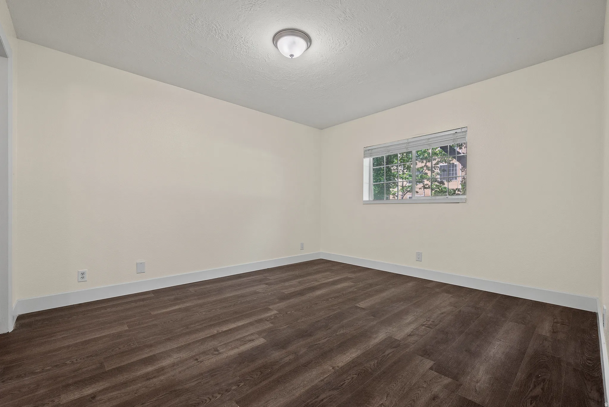 Neutral tone walls with wood-finish flooring, white baseboards, and a single window featuring blinds