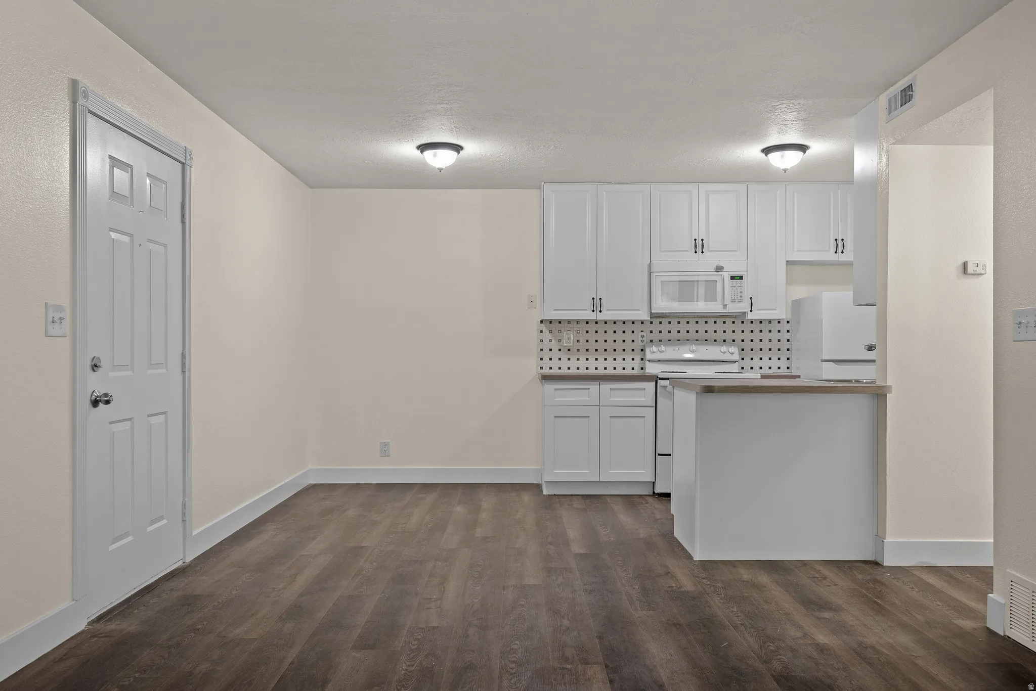 Kitchenette with white cabinetry, built-in microwave, electric range, and a two-tier peninsula