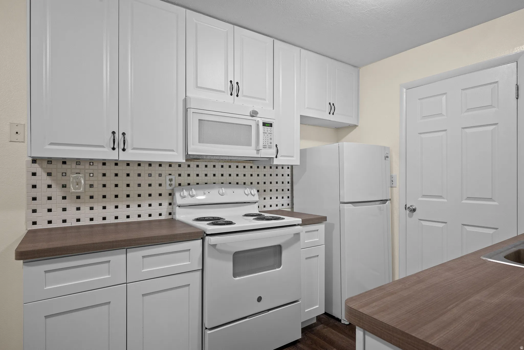 Kitchen featuring white paneled cabinetry, a mosaic tile backsplash, wood-finish countertops, and white appliances