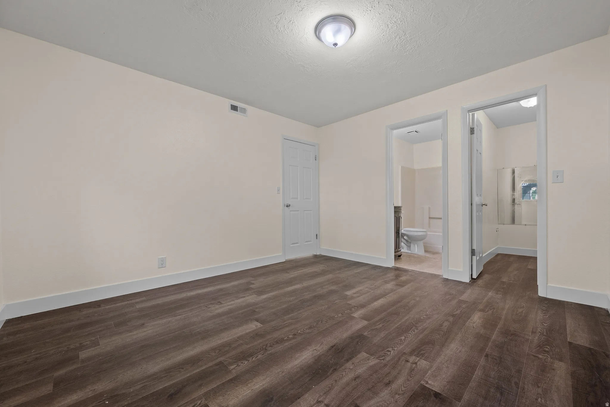 Spacious room featuring wood-finish flooring, light-toned walls, white trim, and a flush mount ceiling light