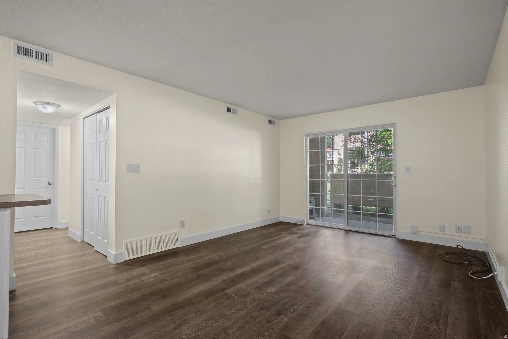 Living area featuring wood-finish flooring, light-toned walls, white baseboards, and a sliding glass door