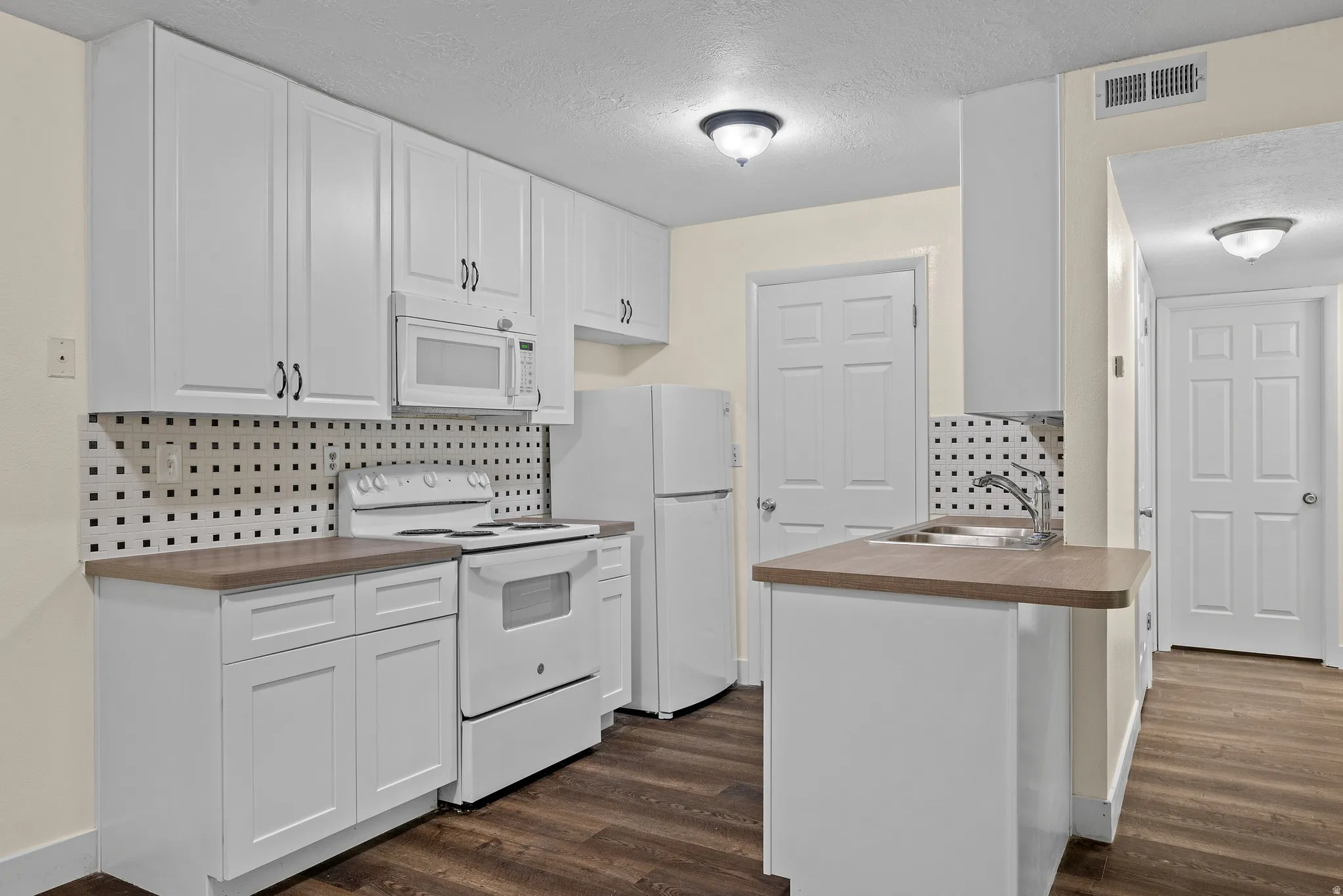 Kitchen featuring white cabinetry, dark wood-finish flooring, a white electric range, a white microwave, and a white refrigerator