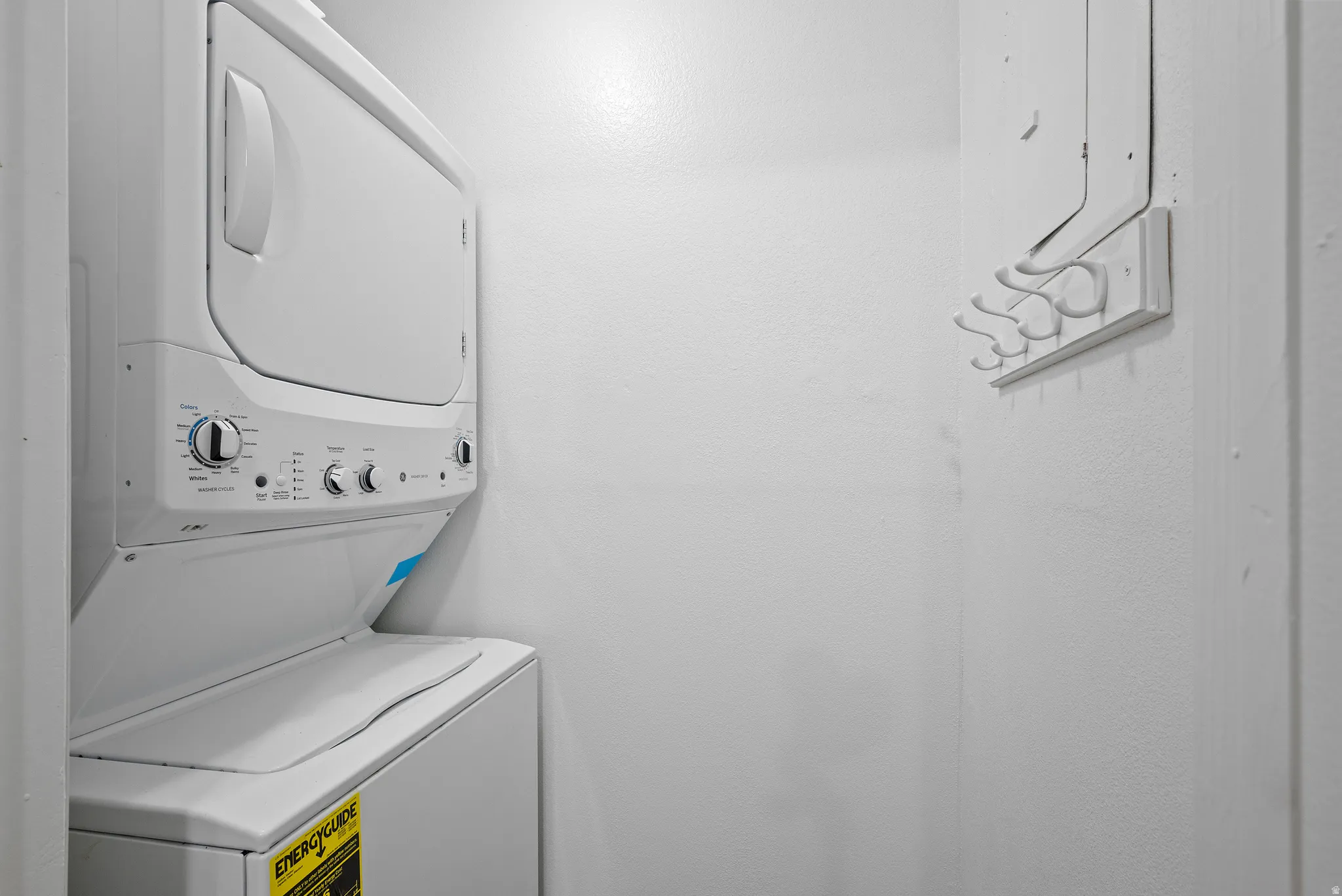 Dedicated laundry area featuring a white stackable washer and dryer unit and a wall-mounted coat rack