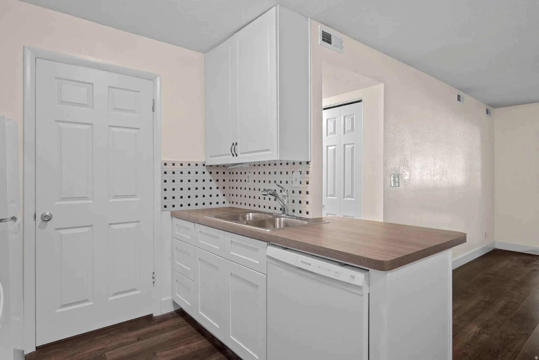 Kitchenette featuring white cabinetry, a double basin sink, a patterned tile backsplash, wood-finish countertops, and dark wood-finish flooring