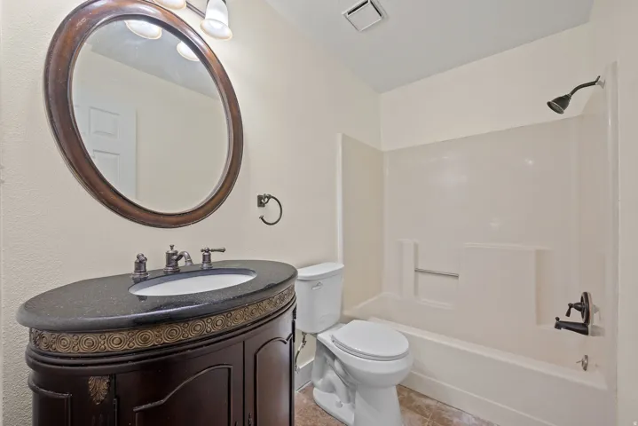 Bathroom featuring a dark wood vanity with ornamental detailing, a black speckled countertop, and an oval mirror with a matching wood frame