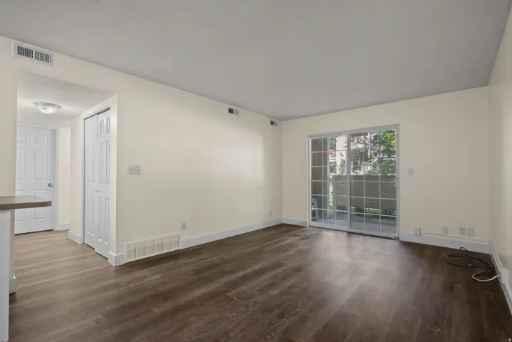 Living area featuring wood-finish flooring, light-toned walls, white baseboards, and a sliding glass door