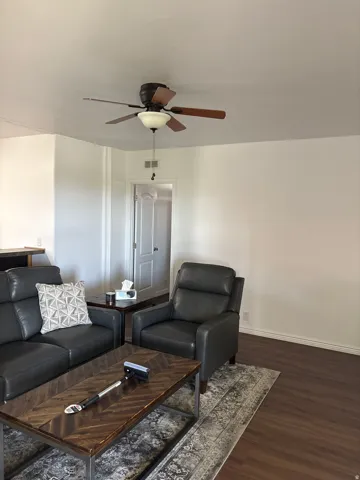 Spacious living area featuring wood-finish flooring, a ceiling fan with integrated lighting, and neutral wall tones