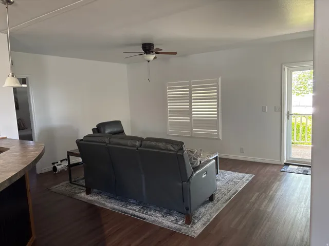 Living area with wood-finish flooring, white walls, and a ceiling fan