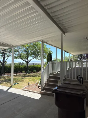 Covered patio with concrete flooring, supported by white metal posts, featuring a white metal roof