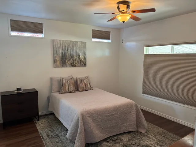 Bedroom featuring a ceiling fan with integrated lighting, wood-finish flooring, and white baseboards