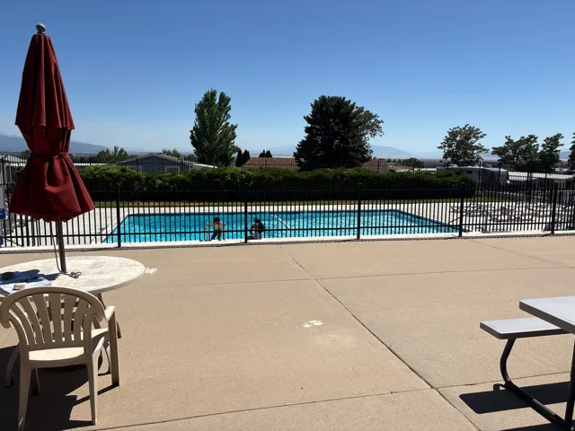 Outdoor swimming pool with a black metal fence surround, bordered by a concrete patio