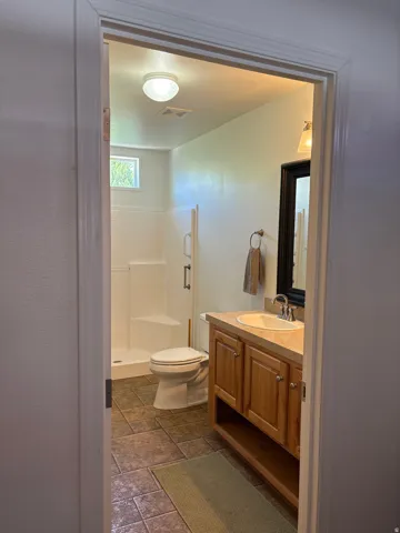 Bathroom featuring a wood-finish vanity with an integrated sink and countertop, a tiled floor, a white toilet, and a stand-up shower with a glass enclosure