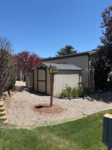 Backyard area featuring a tan storage shed with a dark shingled roof, a rock ground cover, and a manicured lawn border