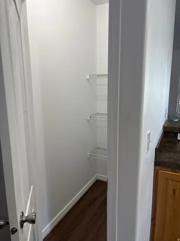 Walk-in storage pantry featuring white wire shelving, wood-finish flooring, and white baseboards