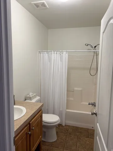 Bathroom featuring a shower-over-tub combination with white subway tile surround, a single vanity with wood-finish cabinetry, a white porcelain sink, and a laminate countertop