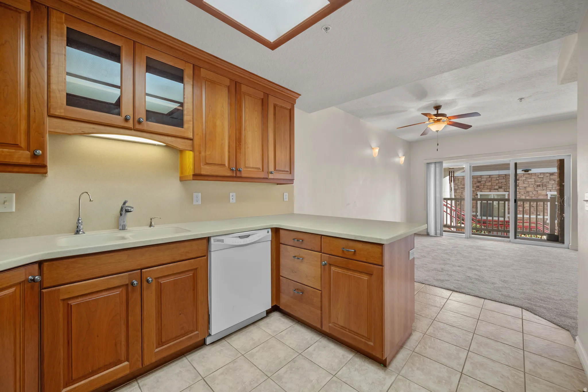 Kitchen featuring warm wood cabinetry, light-toned countertops, tile flooring, and a skylight